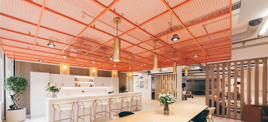 Orange expanded metal ceiling rafts suspended over an office breakout kitchen, concealing services above